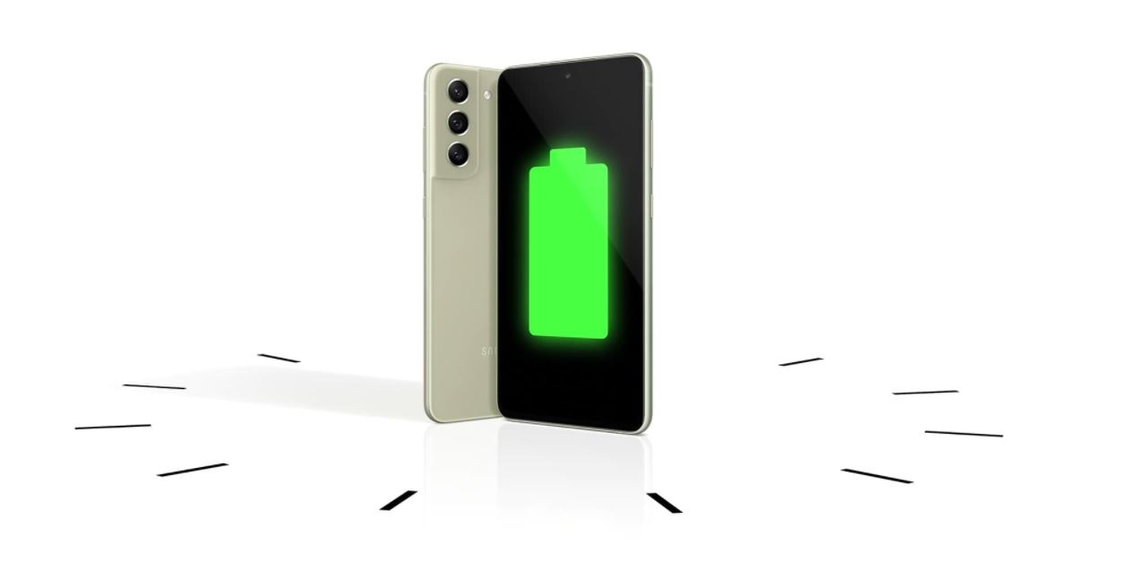 Dois telefones Galaxy S21 Fe 5G vistos em pé, um visto pelas costas e o outro visto de frente com um ícone completo da bateria na tela. Os telefones são colocados em um relógio para demonstrar a longevidade da bateria