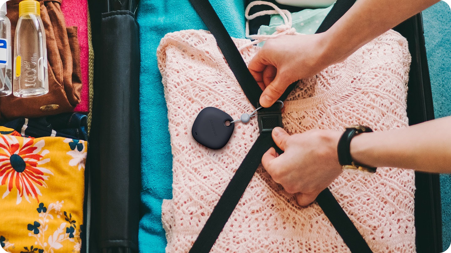 A person attaching a Galaxy SmartTag to the straps inside a suitcase, indicating SmartTag can be tied to important things