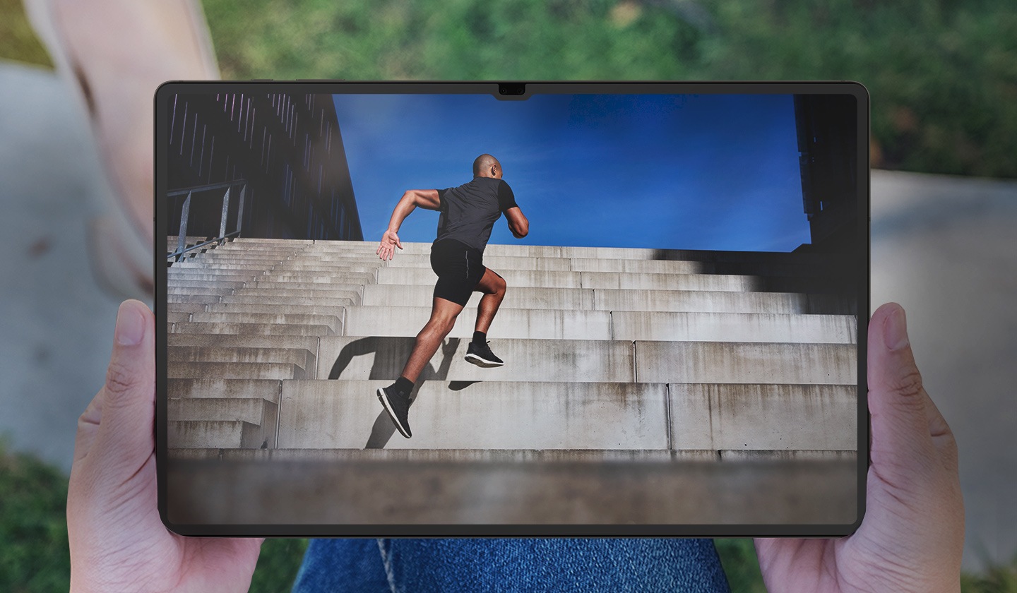 Μπροστινή άποψη ενός Galaxy Tab S9+, το οποίο το κρατάει ένα άτομο σε εξωτερικό χώρο, με θάμπωμα και αντανάκλαση να είναι ορατά στην οθόνη.