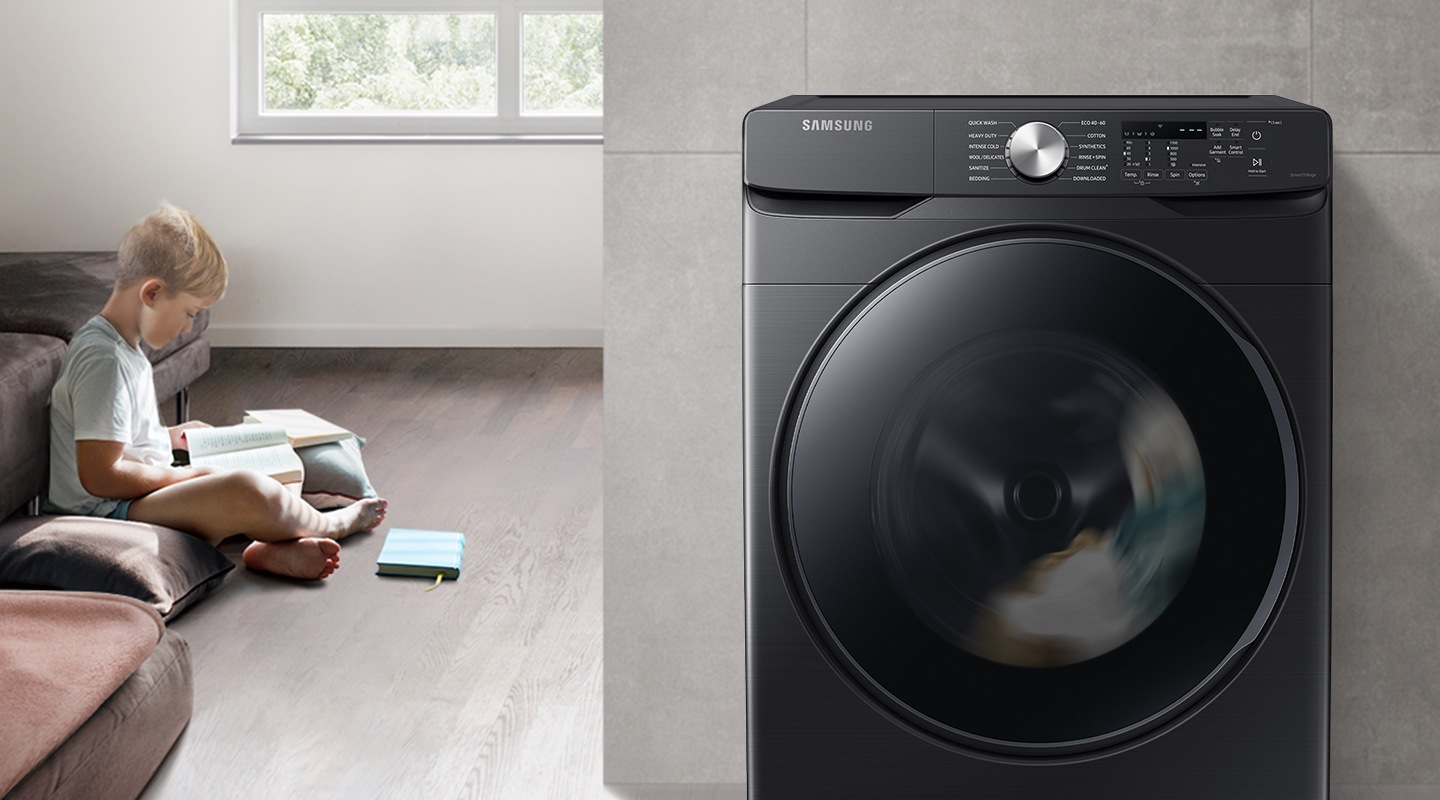 The boy reads the book during the day in the living room, while the washer runs silently next to him.