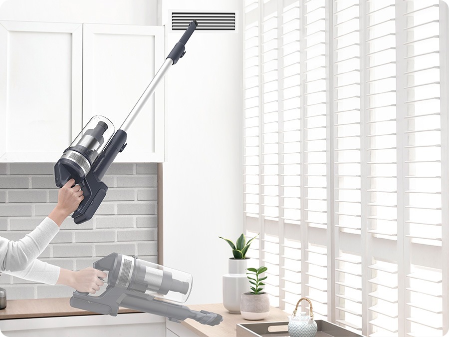 A person lifts Jet 65 with one hand and Cleans vent with the crevice tool and cleans table with the combination tool.
