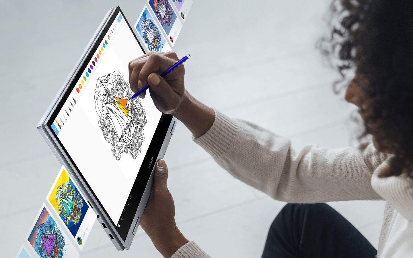Woman uses S Pen to color in a drawing on PENUP with colorful pictures surrounding the laptop.