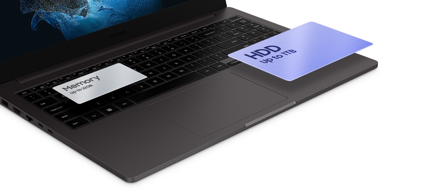 一個石墨色的 Galaxy Book2 打開，從左上角傾斜。 有兩張卡盤旋在底板上。 鍵盤左上角有一張銀色卡片，上面寫著記憶體高達32GB。 紫色卡片位於右下角觸控板旁，上面寫著 HDD 高達 1TB。
