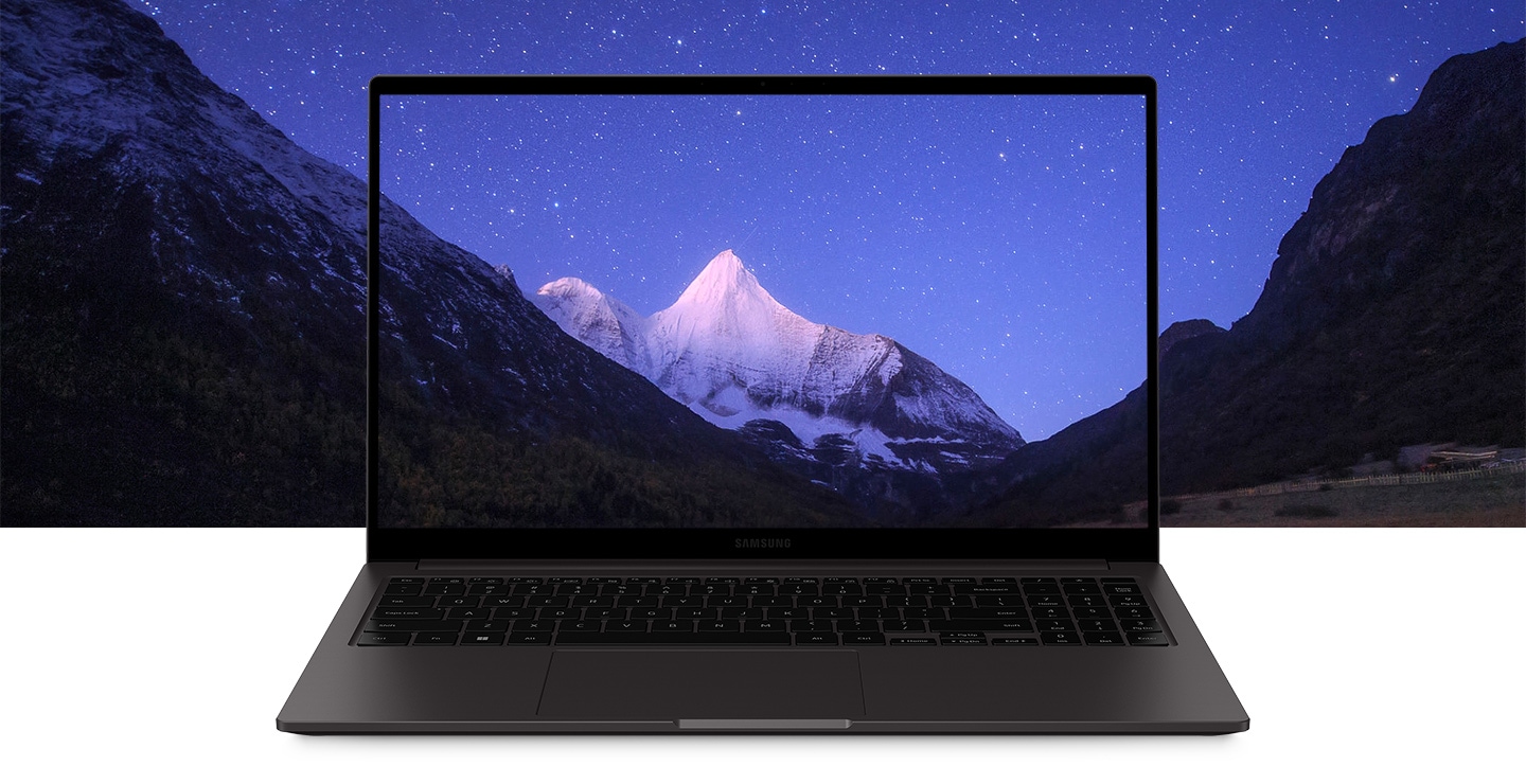 An open graphite-colored Galaxy Book2 is facing forward with a wallpaper of a snow-covered mountain range below a sky full of stars. This wallpaper extends out of the Galaxy Book2’s screen and into the background.