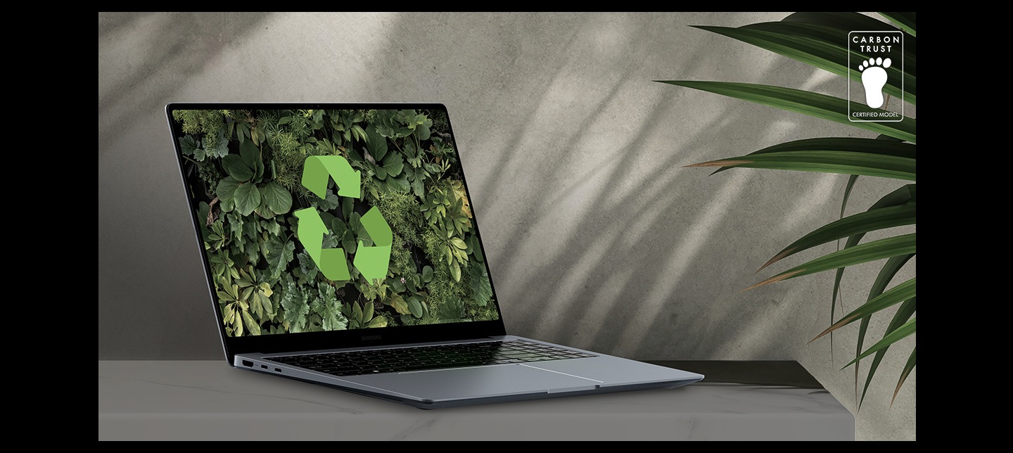 一部月石灰 Galaxy Book4 Ultra 放在桌上，旁邊有棵綠色植物， Galaxy Book4 Ultra  打開並稍稍朝右，屏幕上顯示著綠色的背景牆紙和回收標誌。碳信托認證商標，文字為 「CARBON TRUST. 認證機型」。