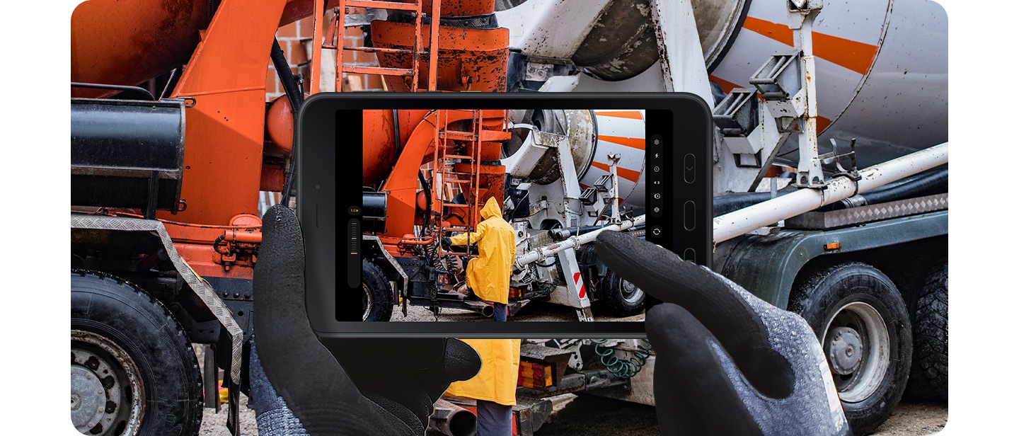 兩隻戴著防護手套的手握住 Galaxy Tab Active5 5G，同時使用相機應用程式捕捉建築工地的場景。