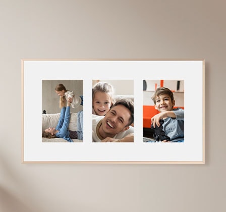 The Frame TV hangs on a wall, displaying three different family pictures on a white matte background.