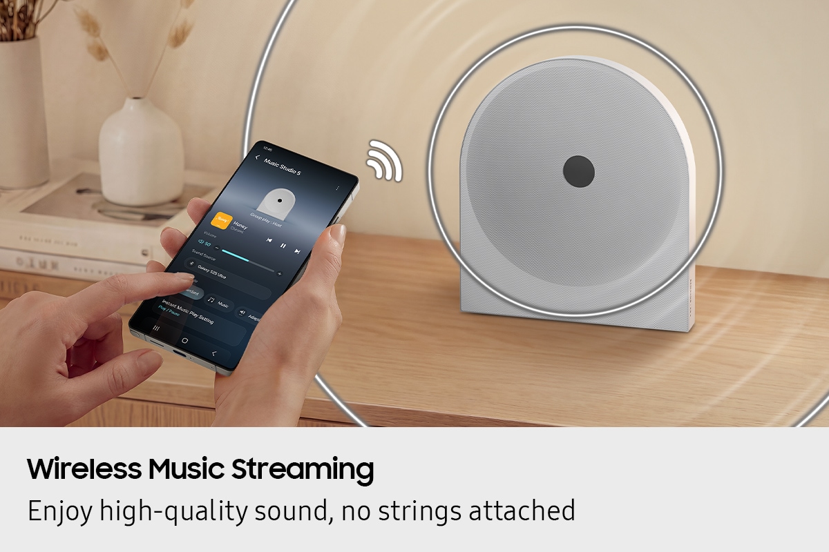 A person uses a smartphone to wirelessly stream music to the Music Studio 5 speaker on a desk, showing easy Wi-Fi and Bluetooth connectivity for seamless music playback.