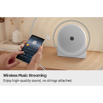 A person uses a smartphone to wirelessly stream music to the Music Studio 5 speaker on a desk, showing easy Wi-Fi and Bluetooth connectivity for seamless music playback.