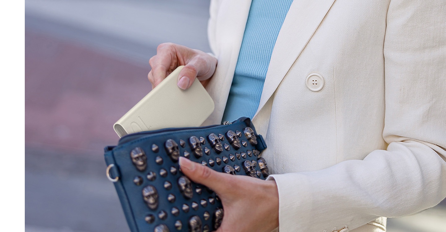 A woman in a beige semi-formal attire holds the beige-coloured battery pack and puts it in her fashionable clutch while on the move.
