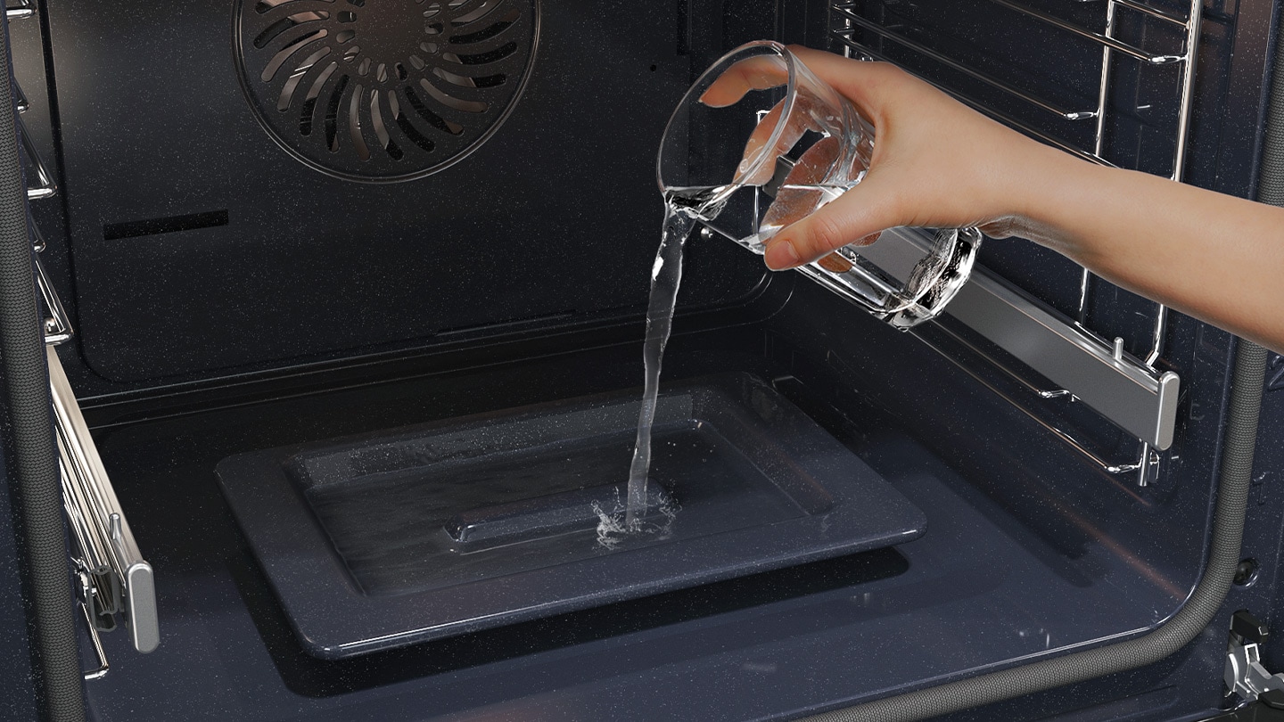 Shows a person pouring water from a glass into a dedicated tray on the bottom of the oven, which is used to create steam.