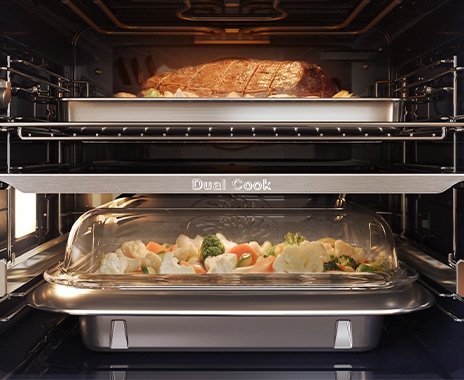 Prikazuje notranjost pečice s peko mesa v zgornjem delu in zelenjavo, ki se kuha na pari v spodnjem.