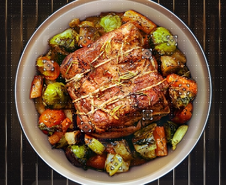 Shows a dish containing a joint of roast meat surrounded by roast vegetables.