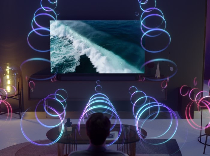 A person is sitting in front of a QLED TV as sound waves fill the room with 3D surround sound.