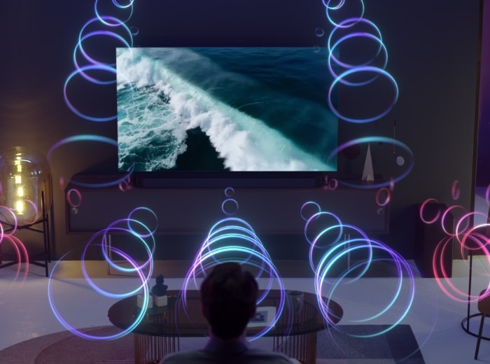 A person is sitting in front of a QLED TV as sound waves fill the room with 3D surround sound.