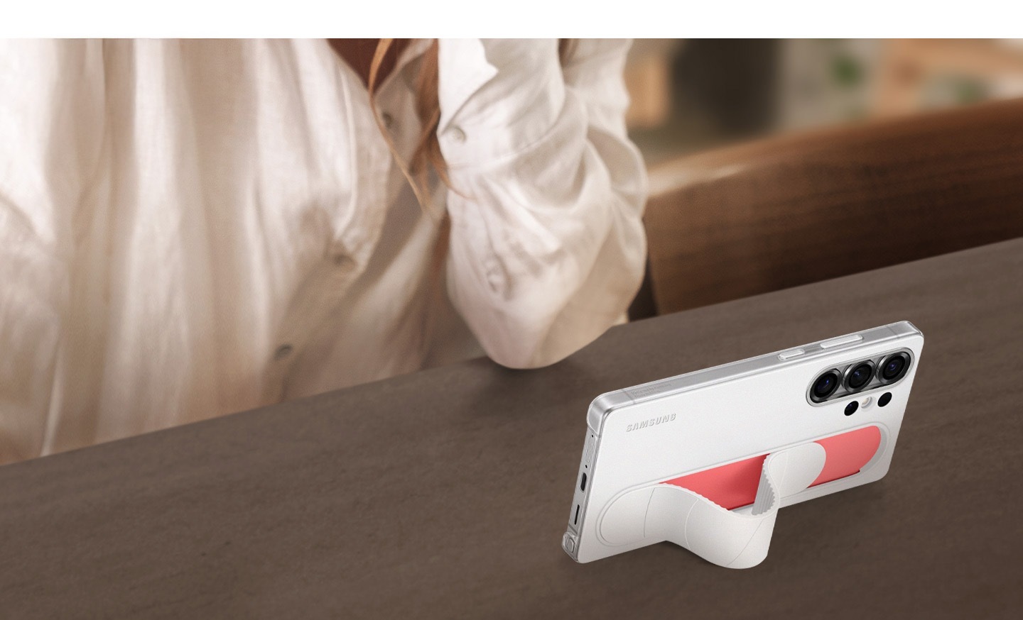Egy Galaxy S25 Ultra készülék fehér színű szíjas álló tokban, enyhén megdöntve látható. Videókat néznek rajta az oldalára döntve.