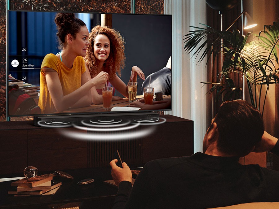 A man is watching his Crystal UHD TV at night with the Soundbar optimally adjusted in Night Mode. The sound from the soundbar's center speaker is emphasized during the night.