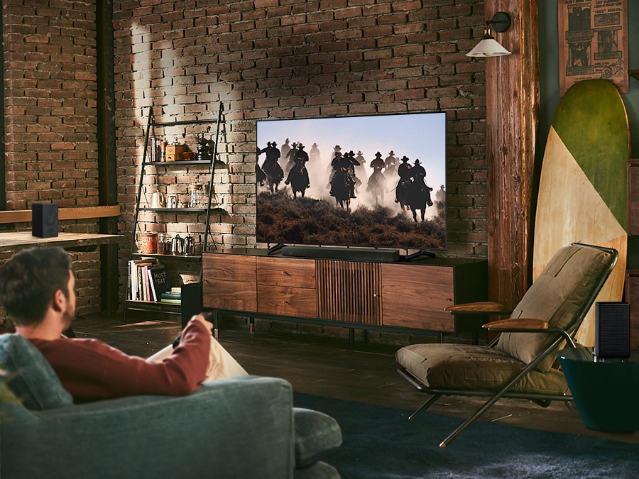 A man enjoys racing content on his TV. Samsung Wireless Rear Speaker Kit and Soundbar create Immersive surround sound. Toggle button is shown.