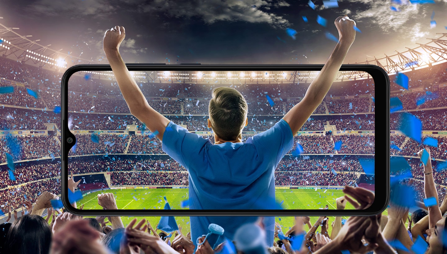 A spectator at a sports event, cheering in the crowd with arms raised up, is shown from the back on Galaxy A04e in landscape. The picture extends outside of the device's screen in all directions to highlight the immersive experience from the display.