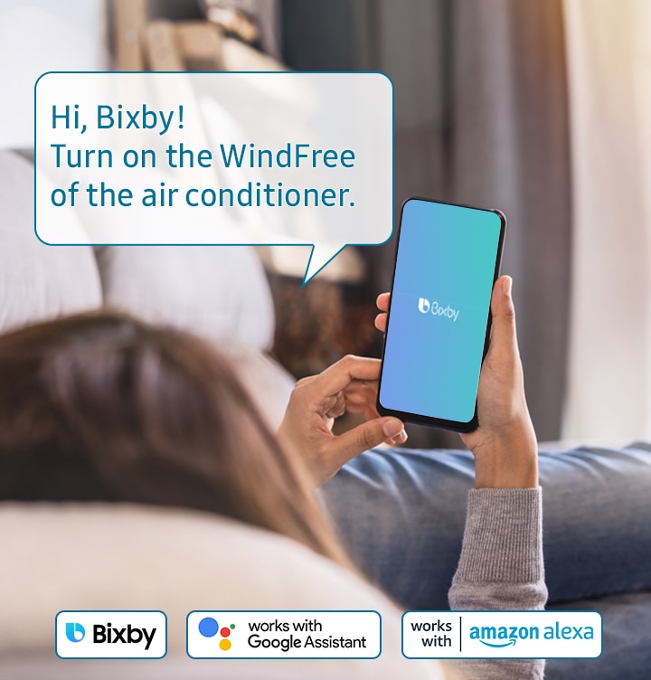 Shows a person relaxing while controlling the air conditioning with their voice using a voice assistant on their smartphone, such as Samsung Bixby, Amazon Alexa or Google Assistant. The example voice command shown says: "Hi, Bixby! Turn on the wind free of the air conditioner."