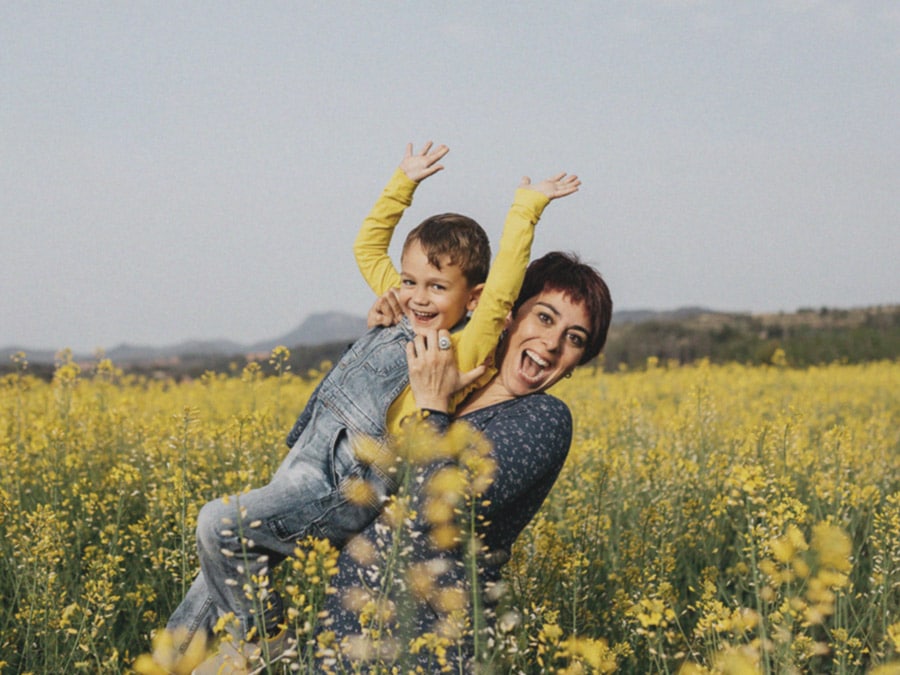A shot of a mother holding her young son in a field of yellow flowers, in low resolution and dulled colors as if it is an old picture.