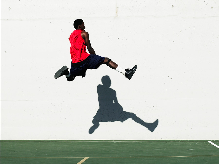 A shot of a man jumping in front of a white wall with his shadow showing against the wall. 