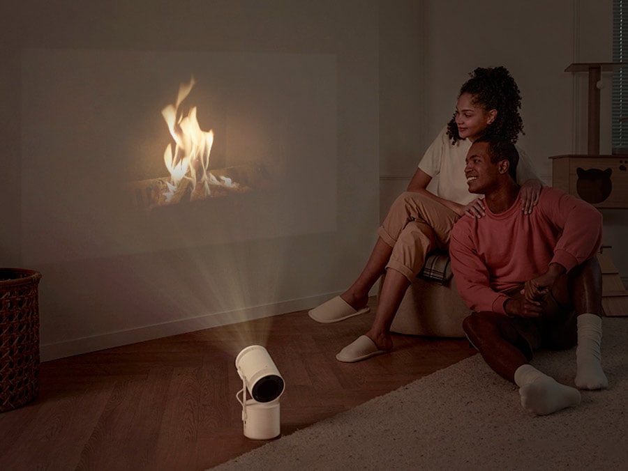 The Freestyle projects an ambient video of a fireplace onto the wall. A happy couple is sitting next to each other.
