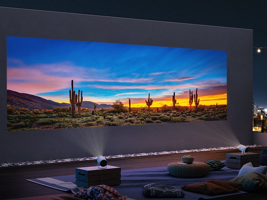 Two of The Freestyle are placed on separate pedestals next to each other in a home theatre, beaming one image of a desert onto a white wall, creating a large screen of up to 170 inches.