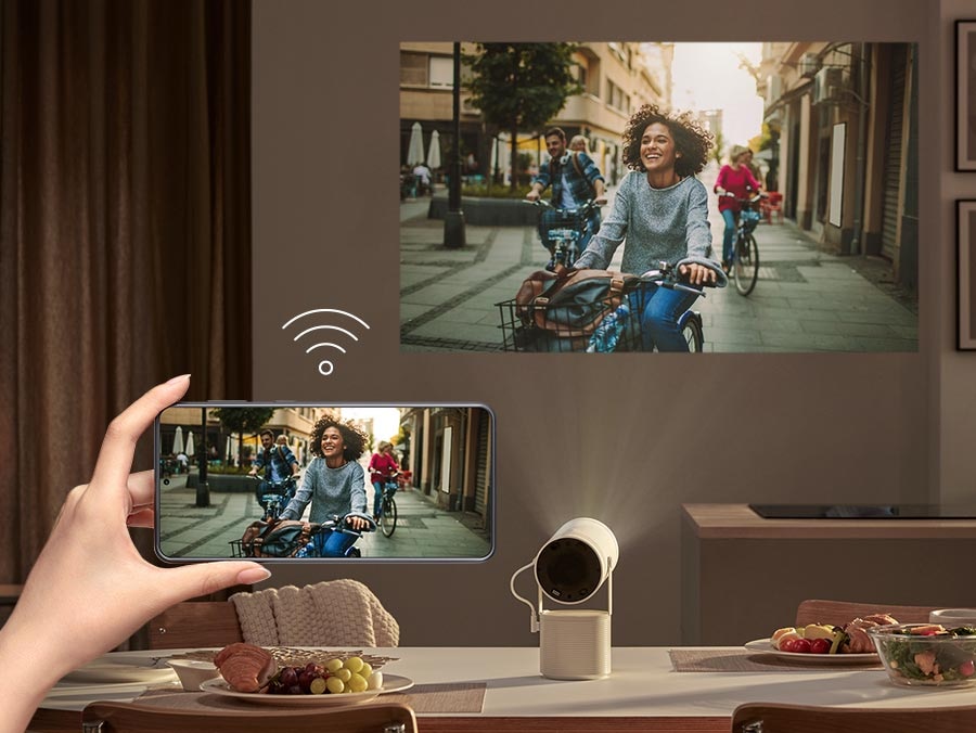 There is a phone with an WI-FI icon above it. The Freestyle beams the same content on a wall that a phone is playing.