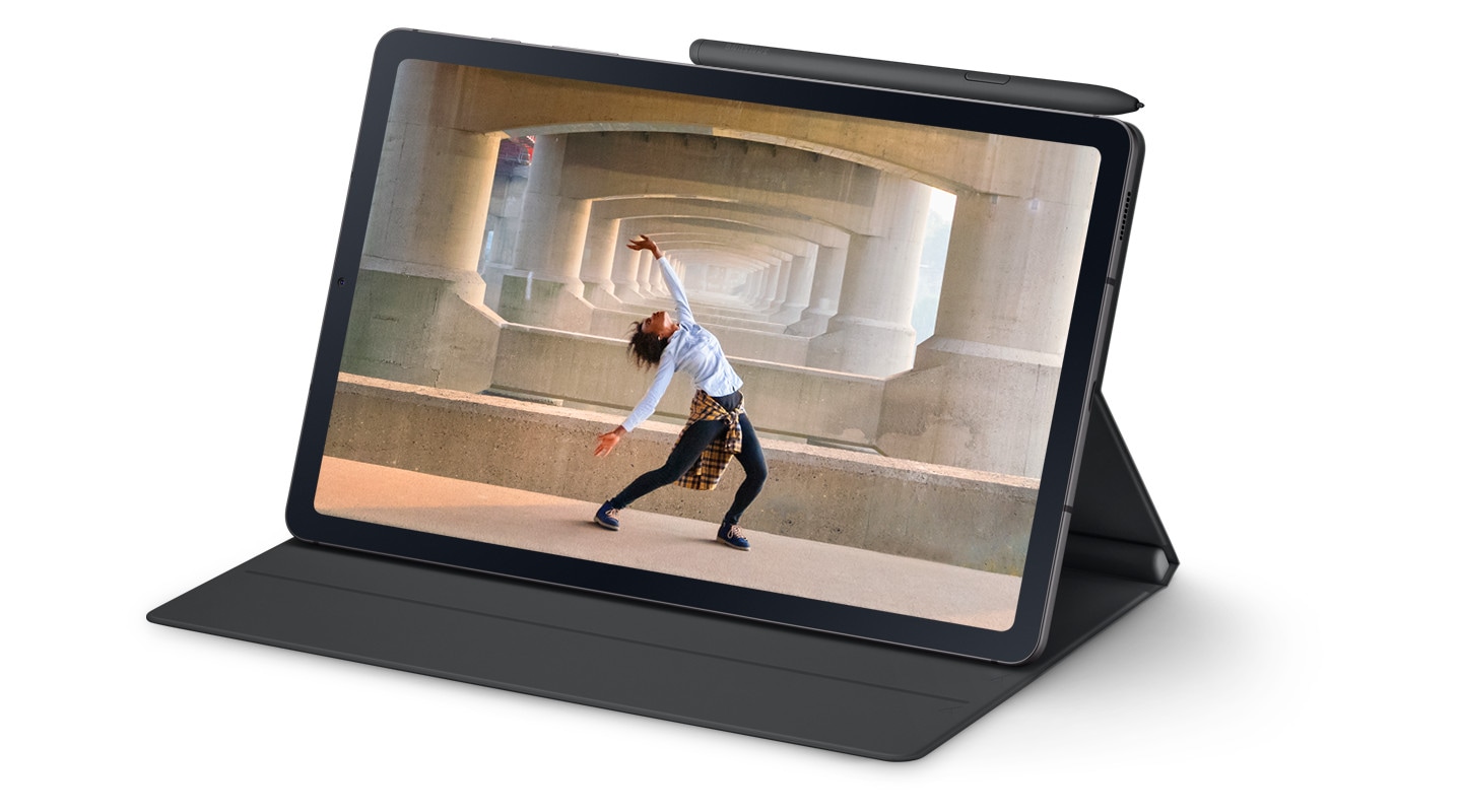 An image of a person dancing under a bridge in an urban setting is displayed full-screen on a Galaxy Tab S6 Lite device. With the Book Cover, the device is fixed in landscape orientation for viewing content with the S Pen attached on top.