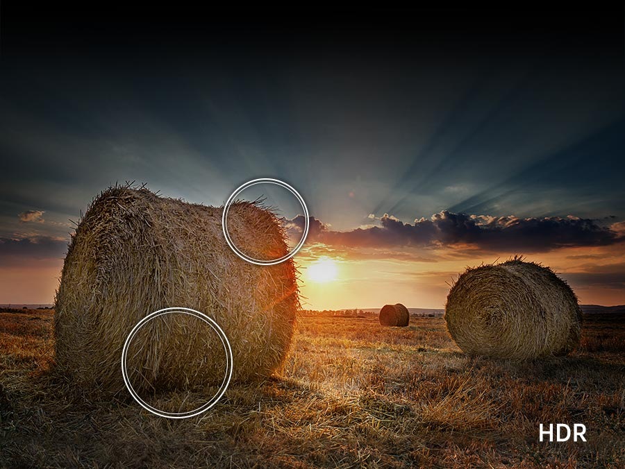 The sun is setting over a wide field with emphasis on a large hay stack. The scene after applying HDR is much brighter and crisper than the SDR version.
