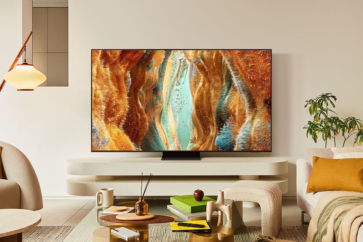 In a cluttered living room, a Samsung Neo QLED TV displays a grassy fantasy landscape on screen.
