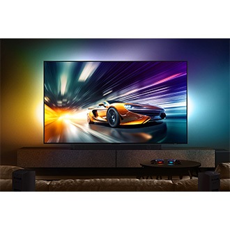 An orange race car is displayed on the QN90D screen in a dark living room with game controllers.