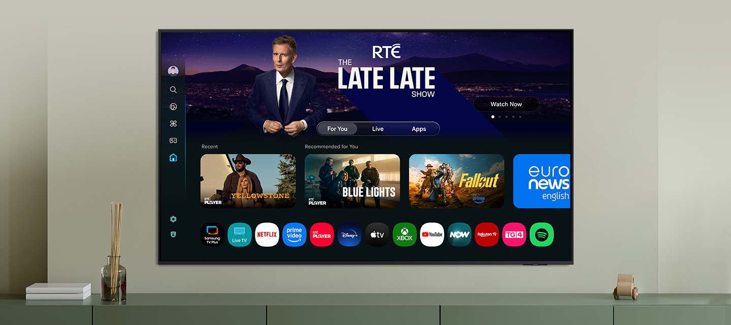One UI Tizen’s home screen, with the various apps and services available, is displayed on a TV in a living room.
