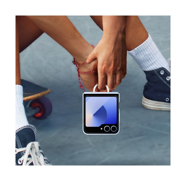 An extreme close-up of a person sitting on their skateboard while comfortably holding their Galaxy Z Flip6 in a Clear Case. The person carries the phone with only their index finger using the easy-carry ring.