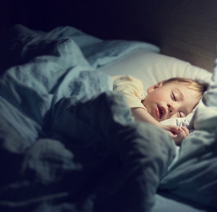 Shows a young child sleeping peacefully in a comfortable bedroom environment.
