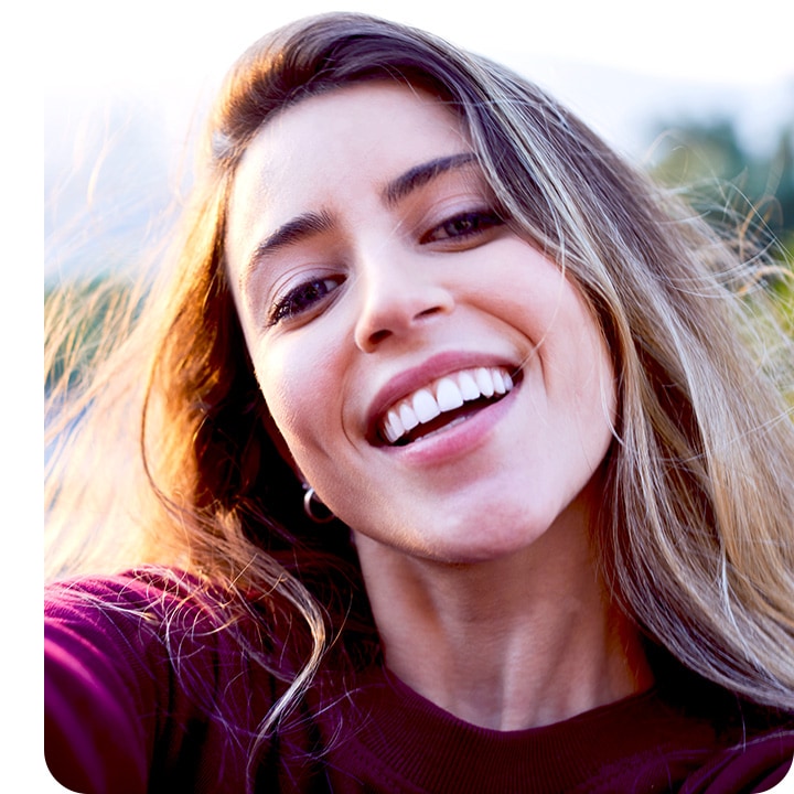 a woman looking into the camera, taking a selfie. the background is subtly blurred out with the bokeh effect.