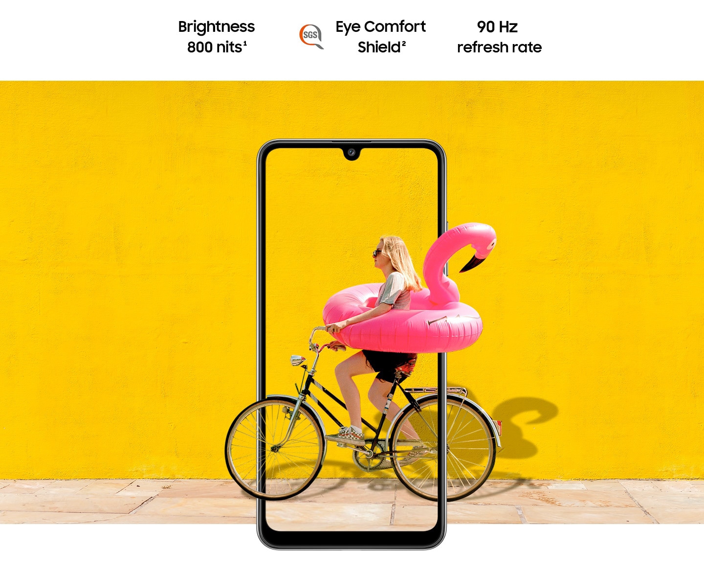 A woman on bike behind Galaxy A32. The picture goes the phone display's edges to represent its immersive view. Text says Brightness 800 nits, Eye Comfort Shield, with the SGS logo and Real Smooth.