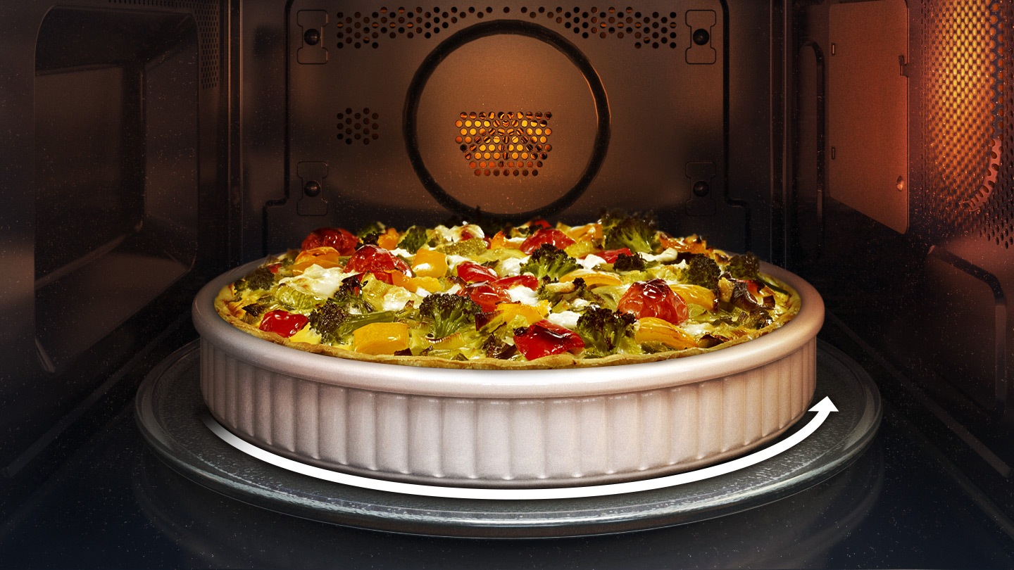 shows the inside of the microwave oven with a round vegetable flan that fits on the turntable. an arrow indicates that the turntable can rotate while the food is being cooked.