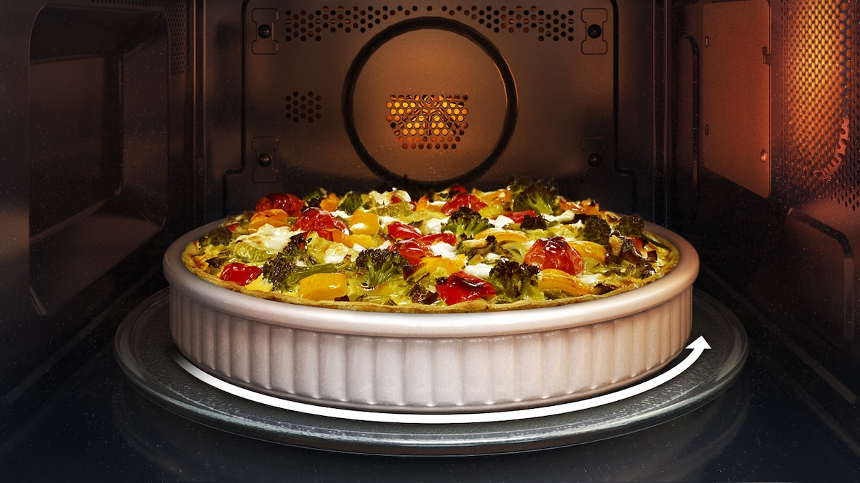 Shows the inside of the microwave oven with a round vegetable flan that fits on the turntable. An arrow indicates that the turntable can rotate while the food is being cooked.
