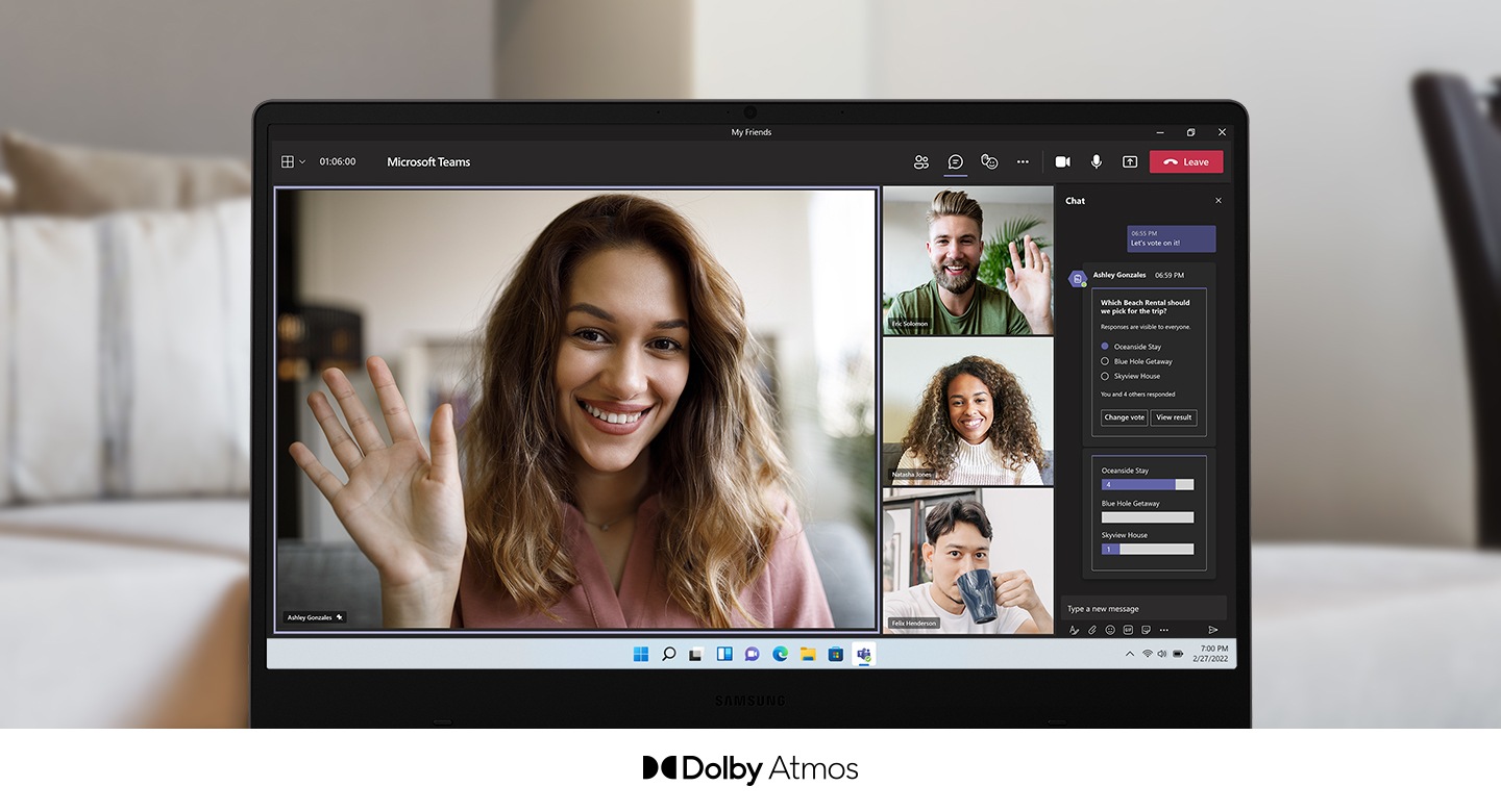 A Galaxy Book2 is facing the front with a video call taking place onscreen. On the left taking up most of the screen, a woman is smiling and waving. To her right are three other participants, two men and a woman. On the far right is a chat room. Below the PC screen is logo for Dolby Atmos.