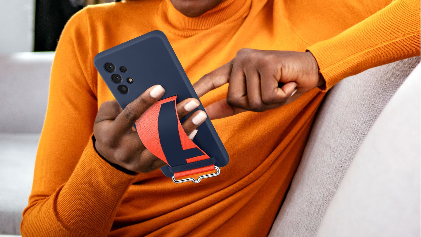 A man is in a comfortable position while using his Galaxy A73 5G wearing a navy Silicone Cover with Strap by holding onto it comfortably with one hand using the strap.