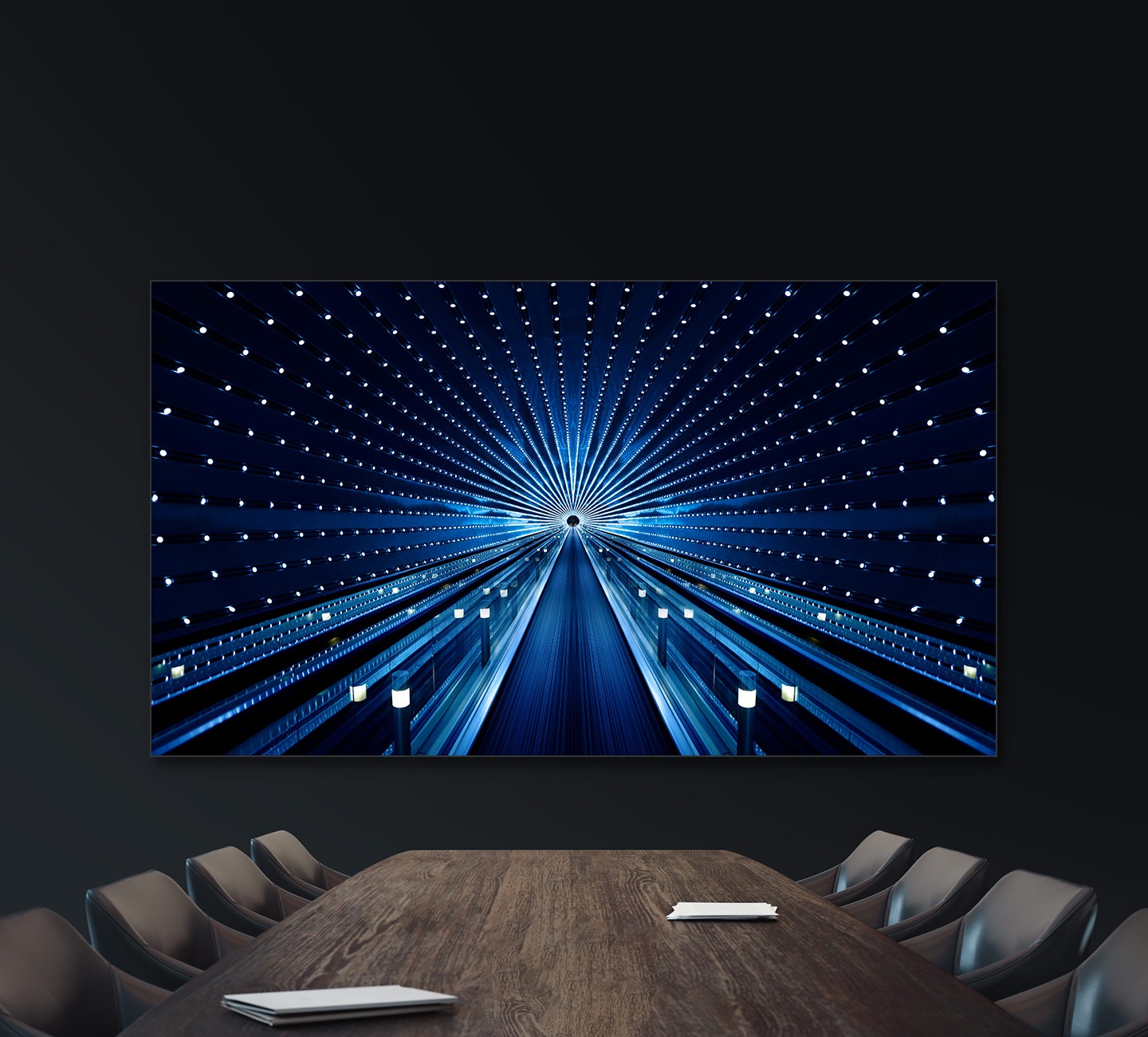 The Wall All-in-One hangs on a wall in a business conference room. A long path surrounded by lights is shown on the screen.