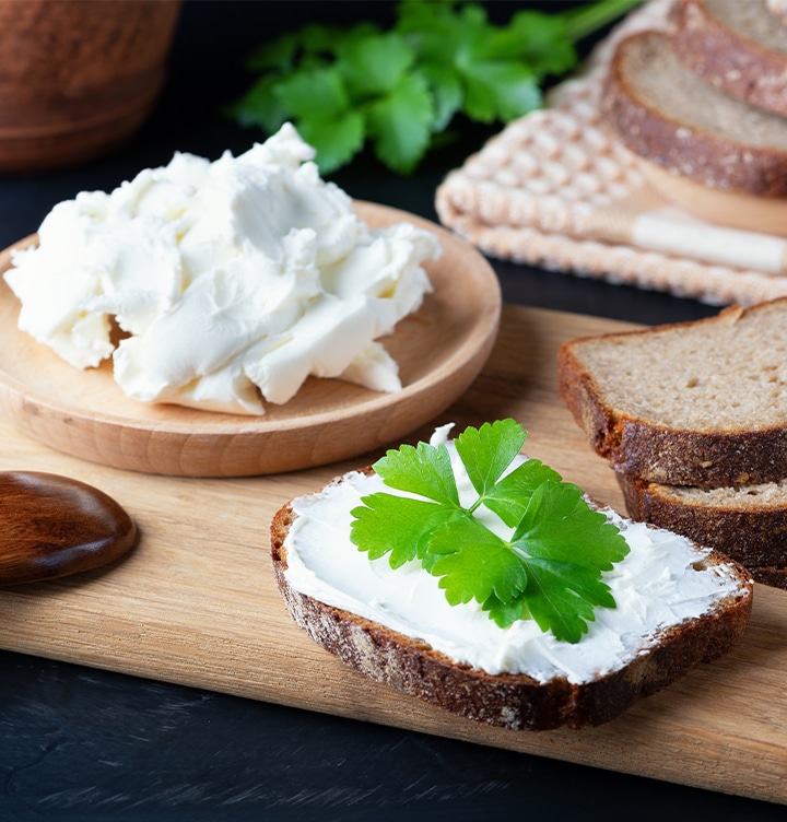 Shows a plate of homemade curd next to some slices of bread. One slice has curd spread on it with a coriander leaf garnish.