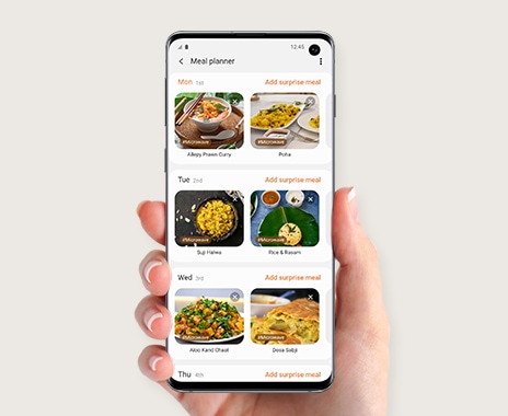 Shows a person holding a smartphone with the SmartThings Cooking app, which is showing a choice of personalized recipes.
