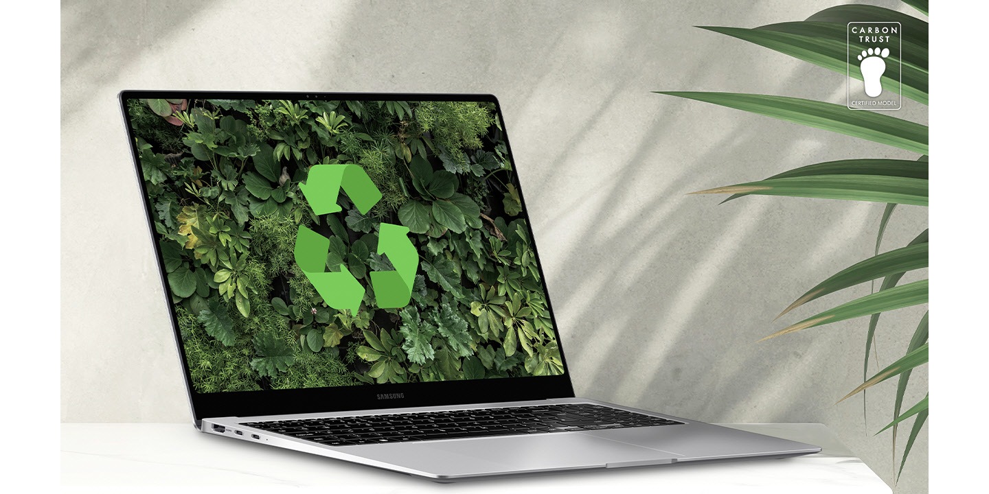 Galaxy Book4 Pro in Platinum Silver placed on a table next to a green plant, open and facing slightly right with a lush greenery wallpaper and recycling logo shown onscreen. Carbon Trust Certification logo with text 'CARBON TRUST. CERTIFIED MODEL.