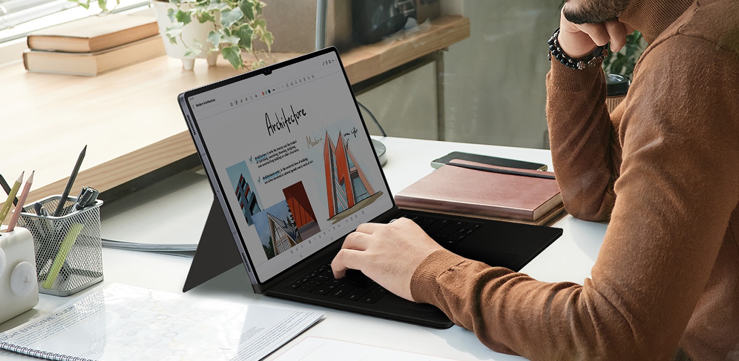 A man is using a Galaxy Tab S10 Ultra with his hand on the keyboard of a Book Cover Keyboard.