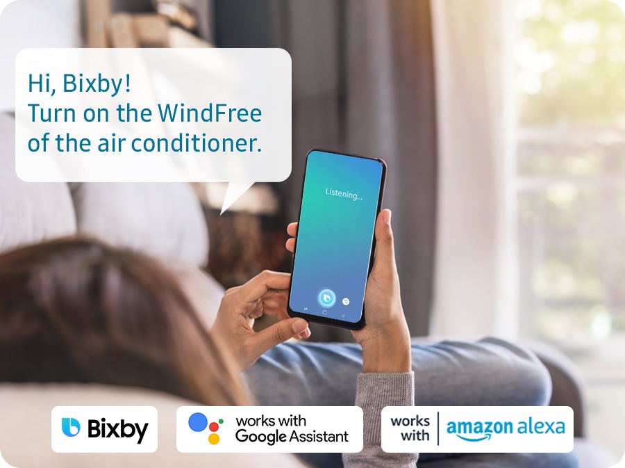 Shows a person relaxing while controlling the air conditioning with their voice using a voice assistant on their smartphone, such as Samsung Bixby, Amazon Alexa or Google Assistant. The example voice command shown says: "Hi, Bixby! Turn on the wind free of the air conditioner."
