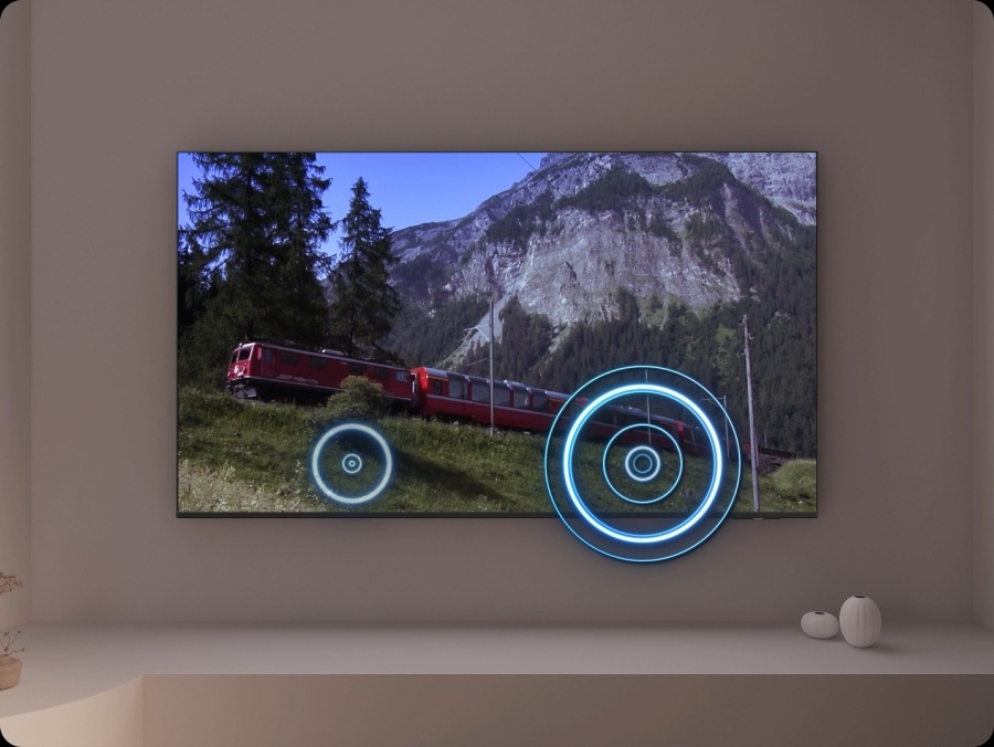 A TV depicts a scene of a train passing by a scenic outdoor location. As it does, sound waves appear near where the train touches the tracks, indicating the noise within the scene.