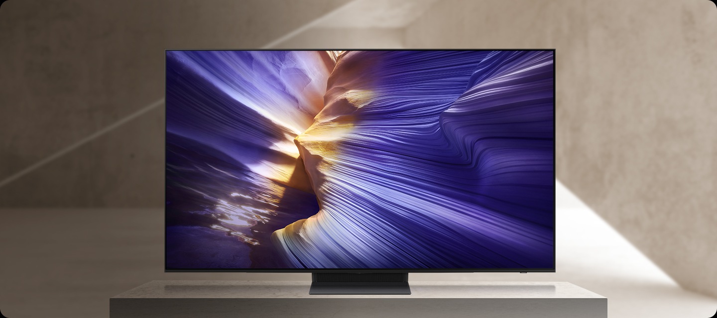 A close-up shot of a corner of a TV. Cut to a close-up shot of the bottom of the TV. Cut to a side perspective of the TV, which is a slim frame like a line. A burst of light travels through the TV frame. The TV rotates around to its front view, to show an abstract purple landscape on screen.